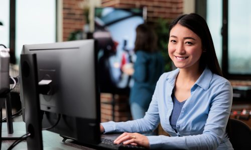 Smiling company employee sitting at desk in office workspace while looking at camera.